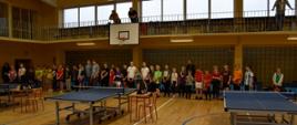 Otwarcie turnieju - na sali gimnastycznej stoją uczestnicy turnieju, przed nimi stoły tenisowe