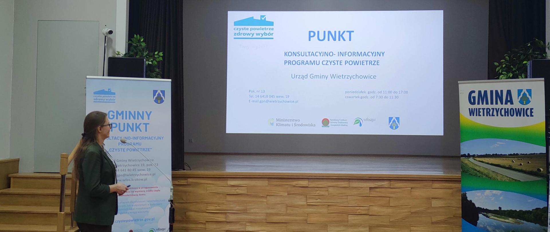 Pracownik Urzędu Gminy na tle ekranu z napisem Punkt Konsultacyjno-Informacyjny Czyste Powietrze Urzędu Gminy Wietrzychowice. W lewym górnym rogu godło RP