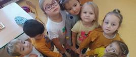 Dzieci z oddziału przedszkolnego stoją w kole blisko siebie i stykają się piąstką prawej dłoni