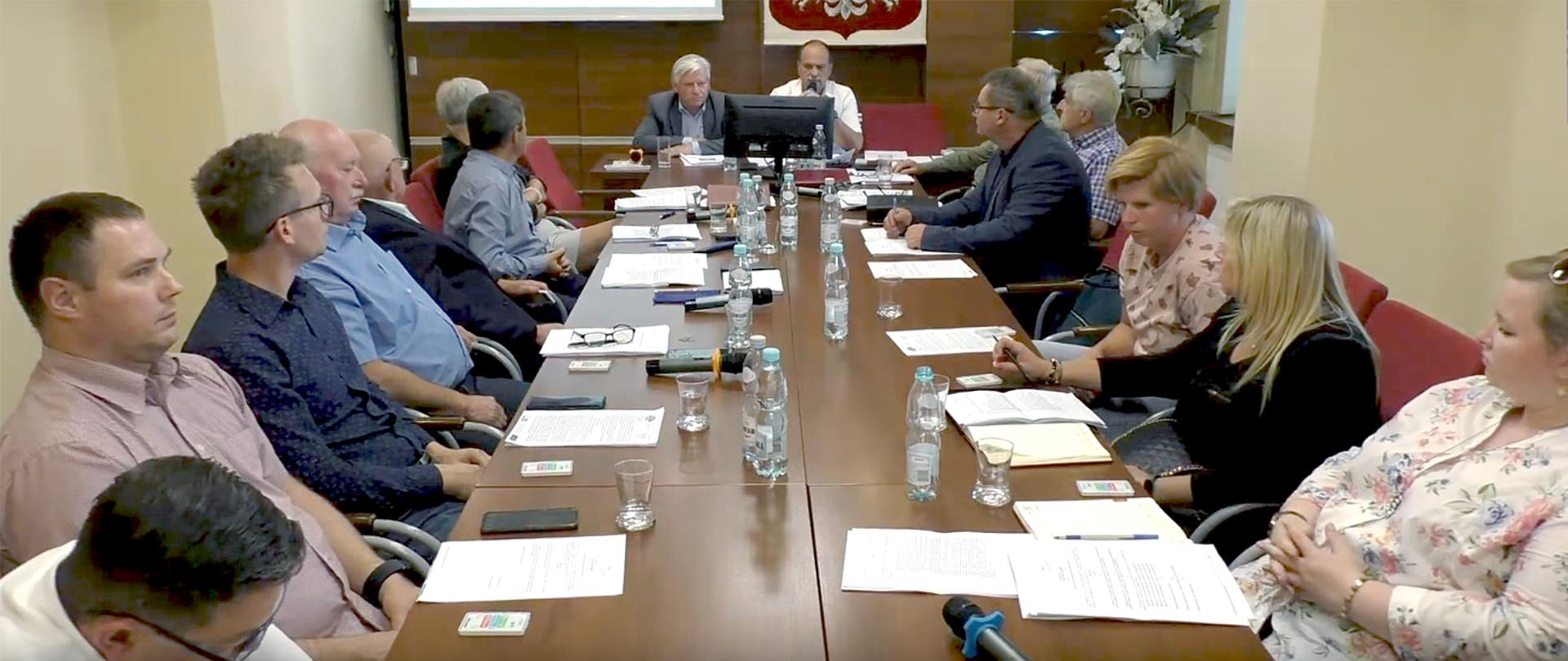 Radni Rady Gminy Kobiór wraz z Wójtem i pracownikami gminy siedzą obradują przy stole. 