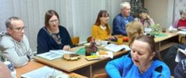 Uczestnicy kolędowania siedzą przy stole, śpiewają