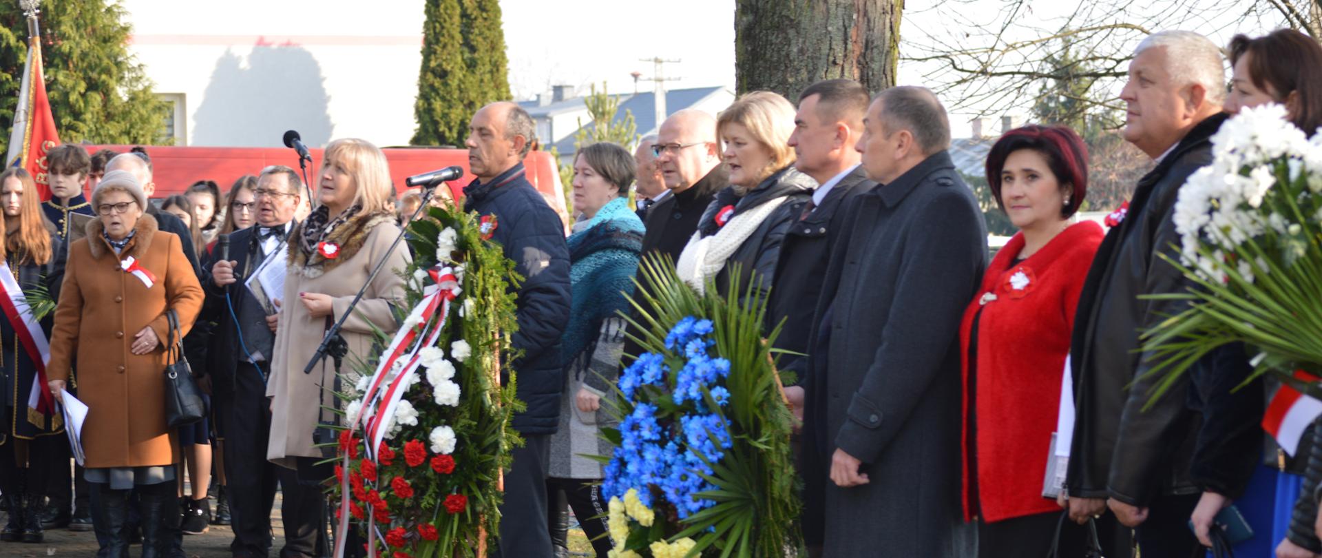 KLub Senior +, Barbara Soszyńska Przedstawiciel GOK, Przewodniczący Rady Gminy Marian Mazurek, Ks. Piotr Chodźko, Wójt Iwona Księżopolska, Delegaci z Ukrainy przed pomnikiem