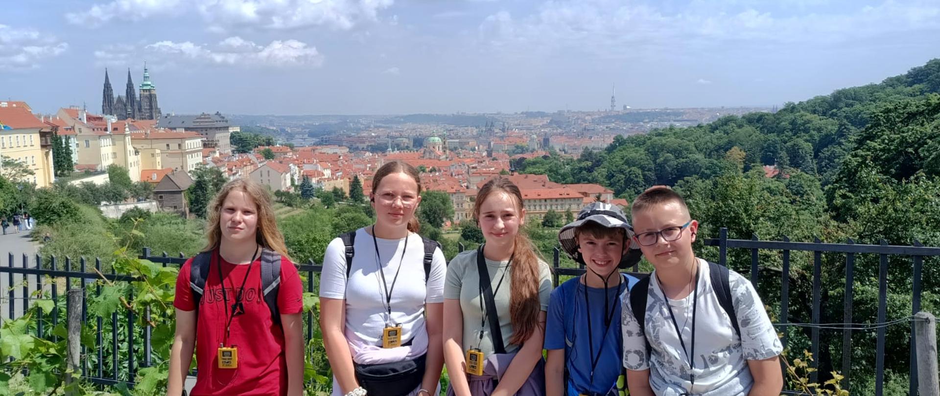 3 dziewczynki i 2 chłopców stoją na wzgórzu, z którego rozciąga się panorama Pragi
