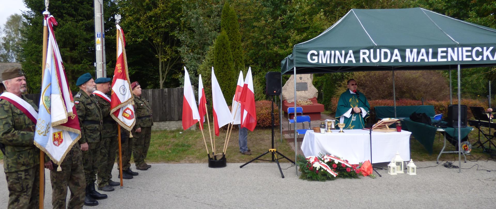 Zdjęcie przedstawia Księdza Proboszcza – Marka Relidzyńskiego celebrującego Mszę Świętą w intencji poległych bohaterów, przed symbolicznym pomnikiem „Tereski”,
w tle służba liturgiczna: kościelny i organista. Z lewej strony przedstawiciele organizacji: Samodzielnego Koneckiego Batalionu im. Hubala oraz Światowego Związku Żołnierzy Armii Krajowej z Włoszczowy i Radoszyc z pocztami sztandarowymi.
