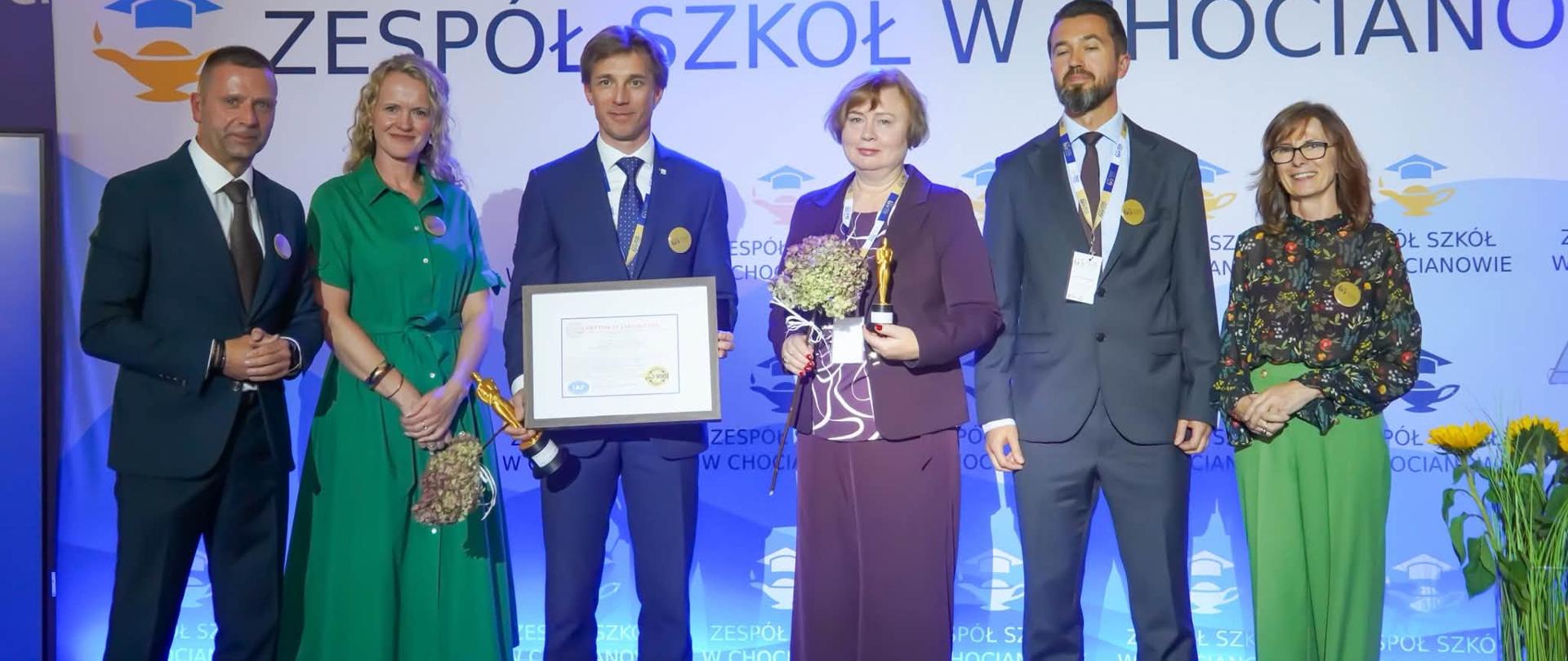 Osoby stoją na scenie i trzymają nagrody