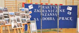 Sala gimnastyczna w Zespole Szkół w Chocianowie. Na podłodze stoją od lewej strony sztalugi ze zdjęciami. Po prawej stronie stoi niebieska plansza informacyjna.