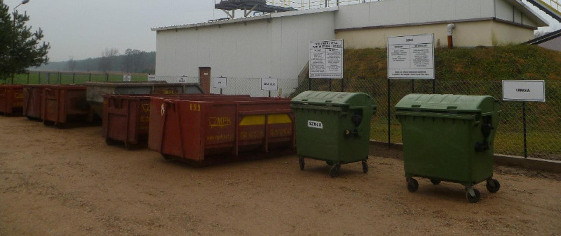 Duże czerwone kontenery oraz dwa zielone pojemniki na śmieci ustawione w rzędzie obok siebie