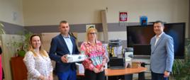 Dwie kobiety oraz dwoje mężczyzn w marynarkach. Za nimi stoi stół z kartonami i laptopem