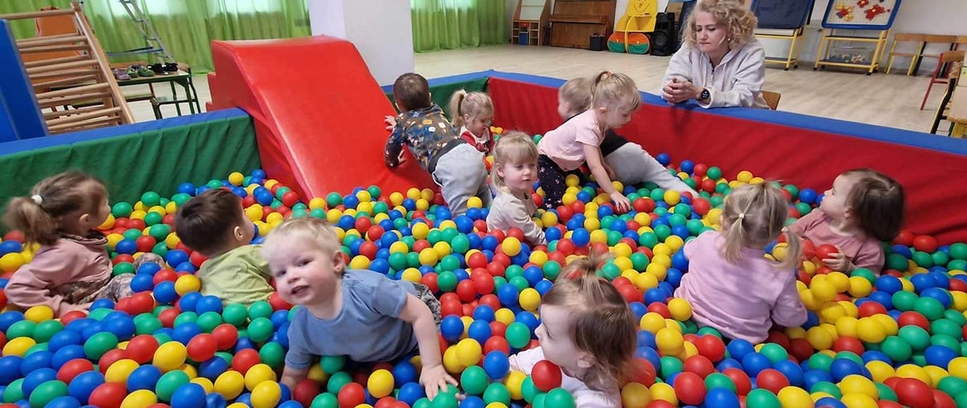 na zdjecu widać basen z kolorowymi kulkami a w nim uśmiechnięte dzieci