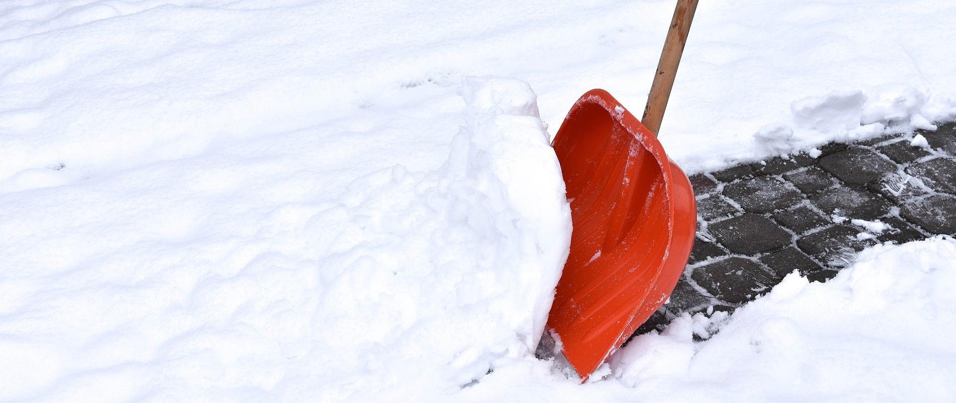 Zdjęcie łopaty do odśnieżania wbitej w śnieg na chodniku.