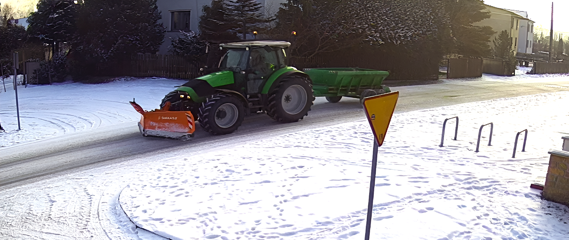 Dzielony traktor z pługiem jedzie na zaśnieżonej drodze