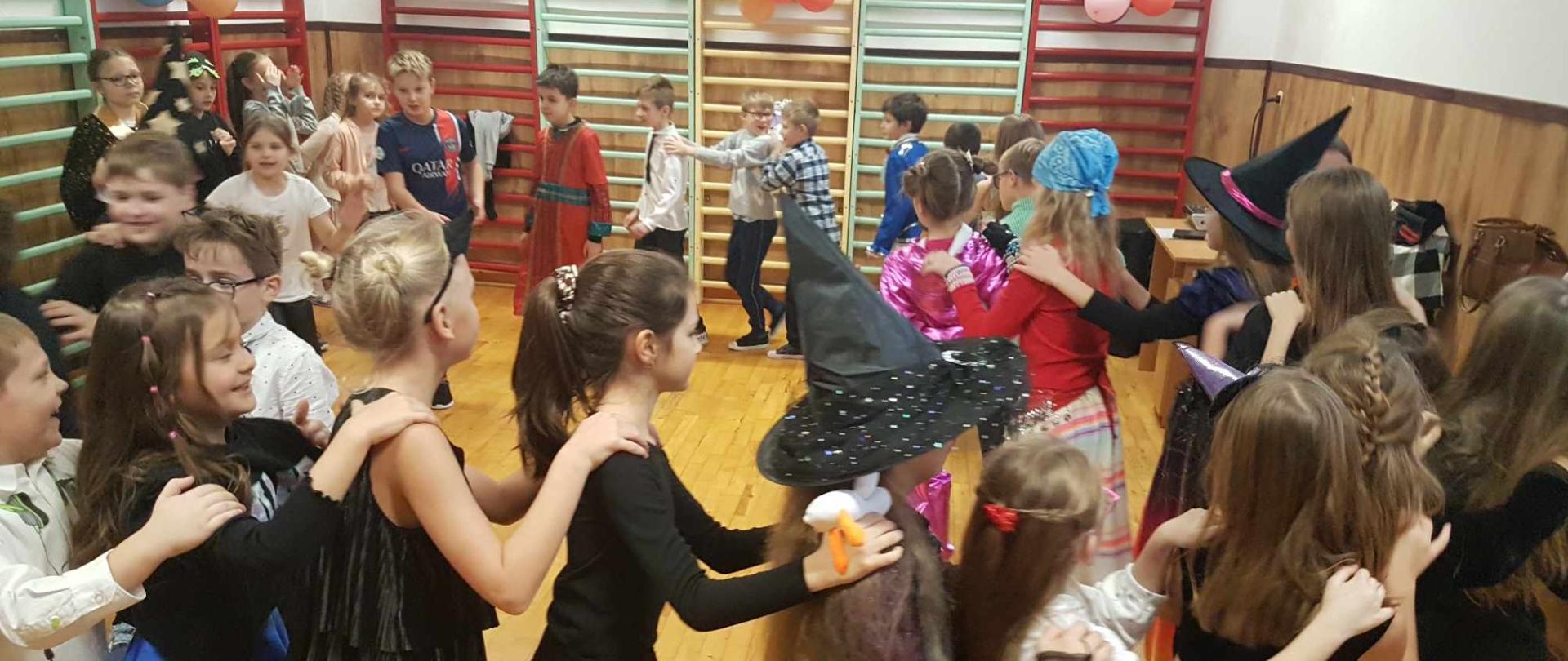 Uczniowie klas młodszych w strojach karnawałowych uczestniczą w zabawach przygotowanych przez wychowawców.