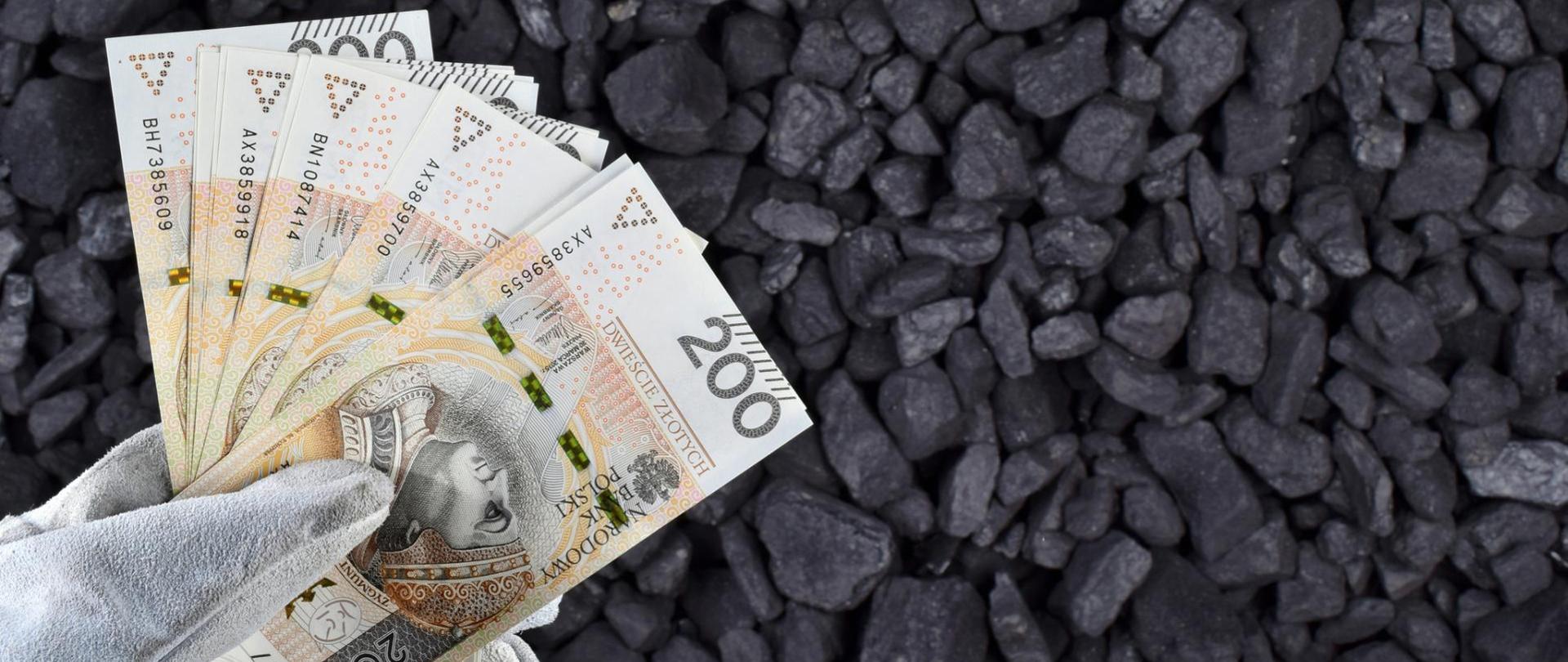 Zdjęcie banknotów dwustu złotowych na tle bryłek węgla. 