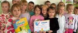 Grupa przedszkolaków pozuje do zdjęcia z dyplomem i wygraną grą zręcznościową
