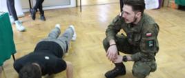 Uczeń wykonuje pompki w asyście przedstawiciela uczelni mundurowej
