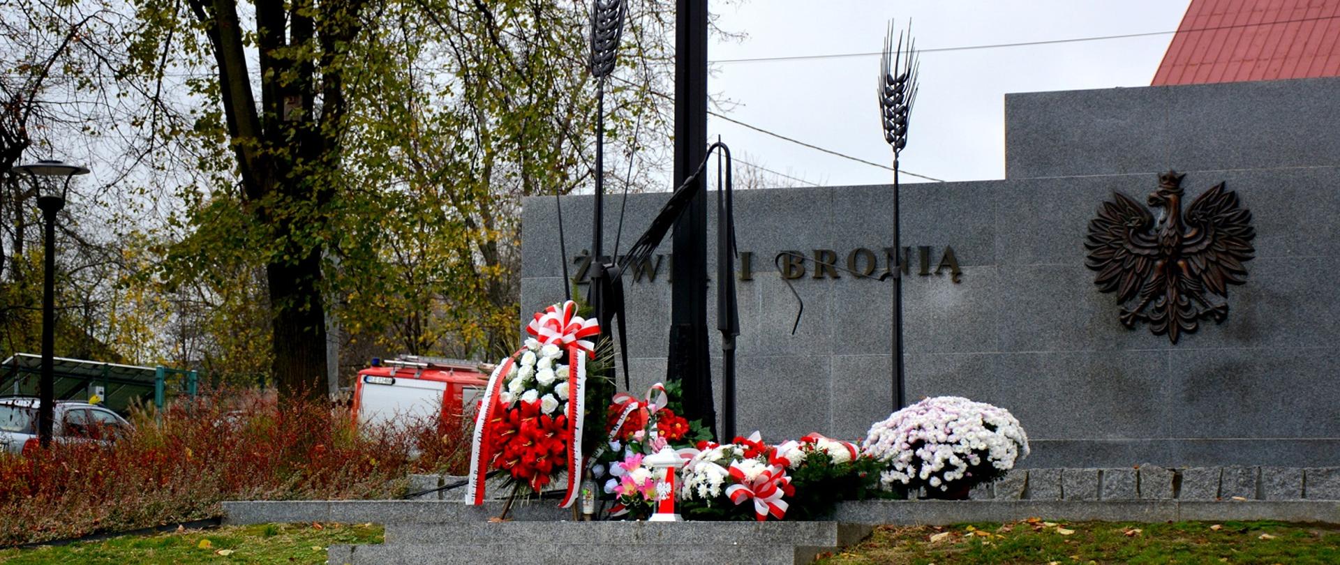 szary pomnik,, przed pomnikiem kwiaty biało czerwone 