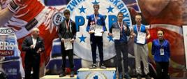 Zwycięzcy w zawodach w Kickboxingu stoją na 3-stopniowym podium, na szyi mają medale, w ręku dyplomy, nasz uczeń stoi na stopniu z numerem 3