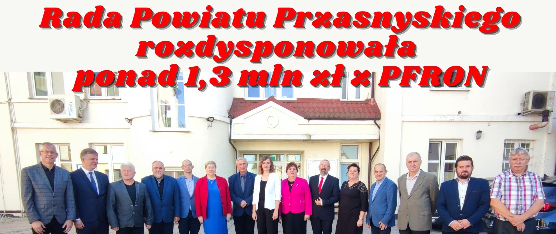 Grafika promująca informację o rozdysponowaniu przez Radnych Radny Powiatu Przasnyskiego ponad miliona trzystu tysięcy złotych z Państwowego Funduszu Rehabilitacji Osób Niepełnosprawnych. Na zdjęciu Radni Rady Powiatu Przasnyskiego stoją na dziedzińcu Starostwa Powiatowego w Przasnyszu przed wejściem do siedziby. 