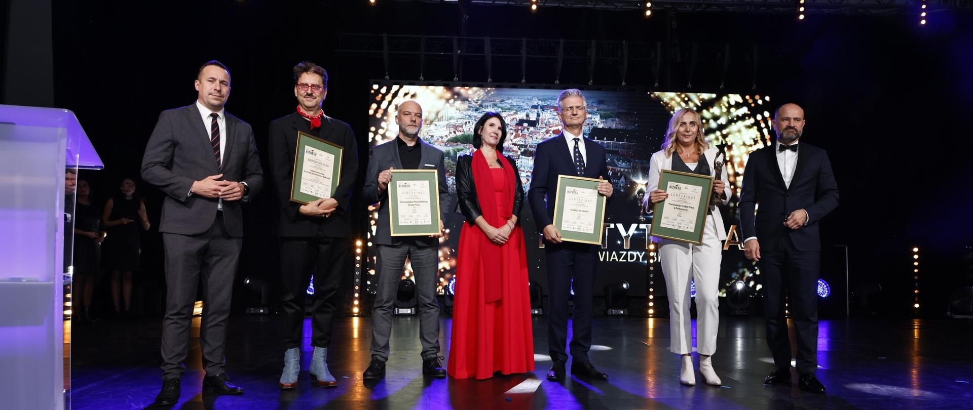 kilka osób w eleganckich ubraniach odbiera nagrody na scenie 