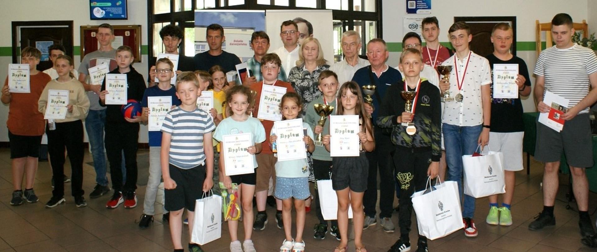 Zdjęcie grupowe wszystkich uczestników biorących udział w XVII Mistrzostwach Diecezji Drohiczyńskiej w Szachach, które odbyły sią w Zespole Szkół Salezjańskich w Sokołowie Podlaskim. Dzieci prezentują dyplomy, medale i nagrody rzeczowe.