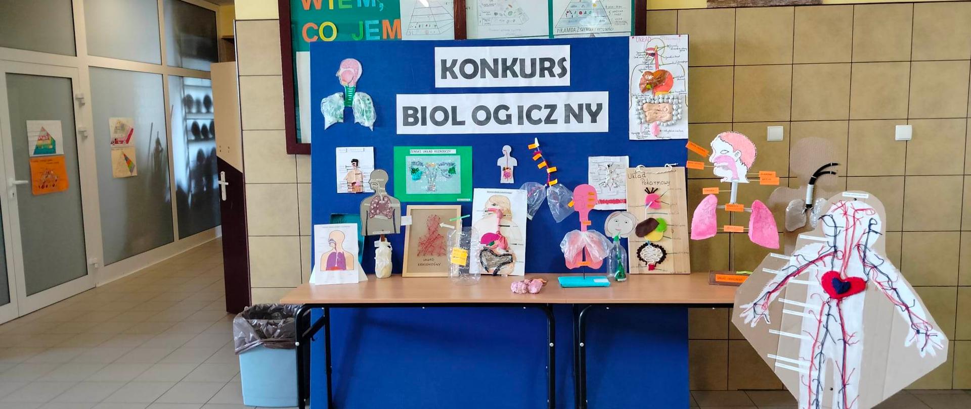 Niebieska tablica i stoli przed nią na których są prace plastyczne 