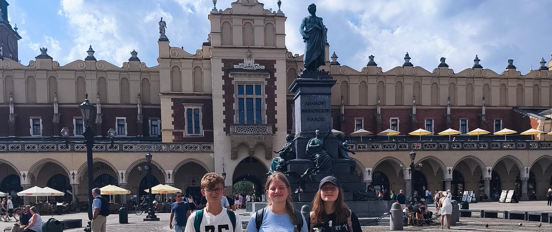 Uczniowie stoją przy pomniku Adama Mickiewicza przed Sukiennicami w Krakowie