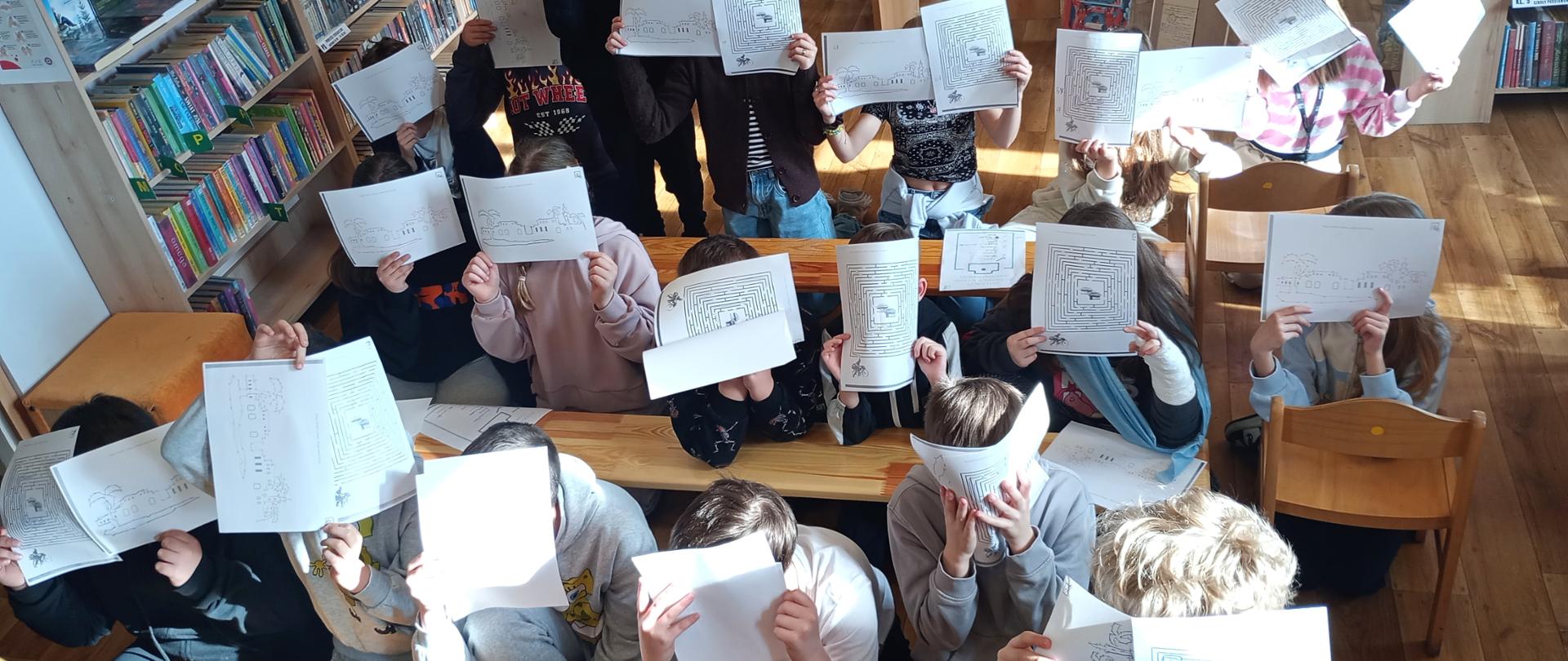 Na zdjęciu widać dzieci pozujące z kartami pracy, na których rysowali oazy i szukali drogi w labiryncie