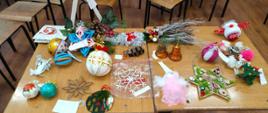 Na stoliku leżą przyniesione przez uczniów na konkurs plastyczny różne ozdoby choinkowe: kule, gwiazdki, aniołki, inne