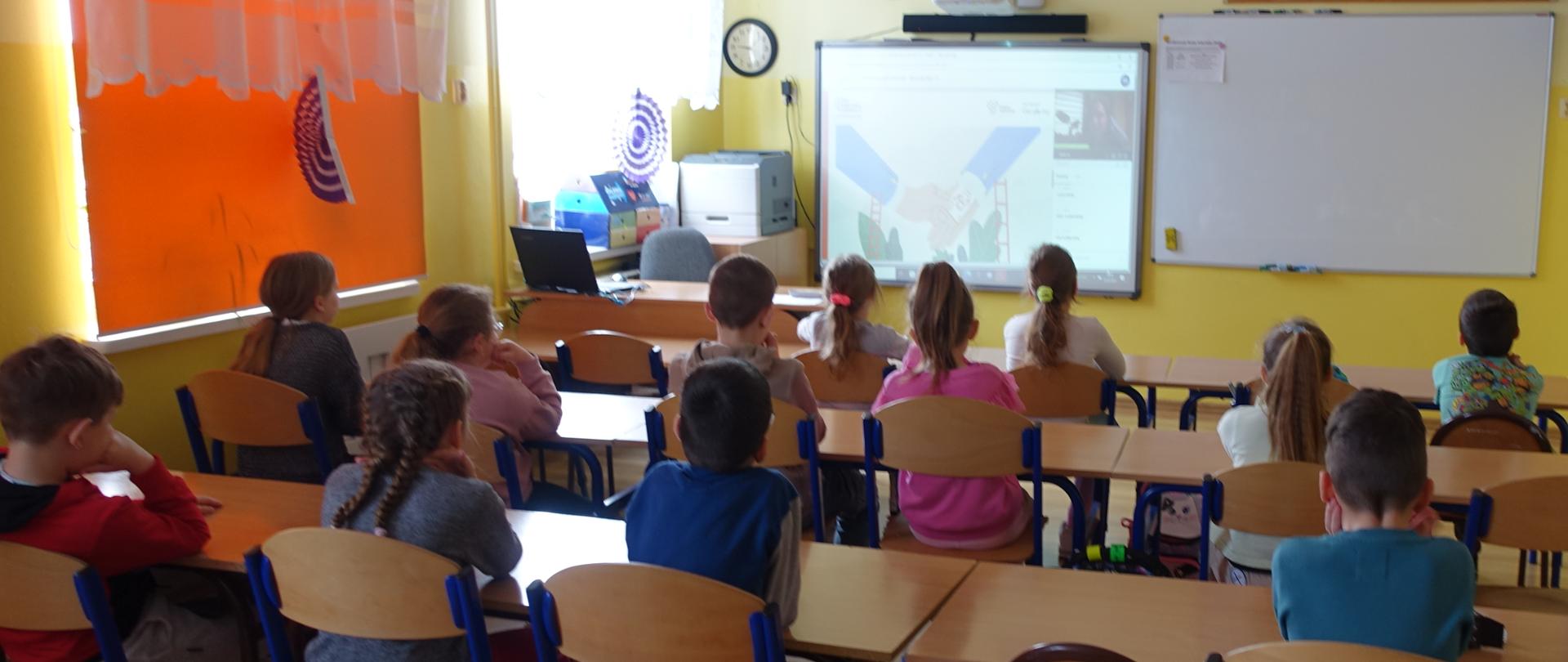 Uczniowie klas I-III w sali lekcyjnej biorą udział w konferencji