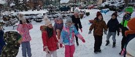 Dzieci ubrane w zimowe kurtki chodzą po śniegu