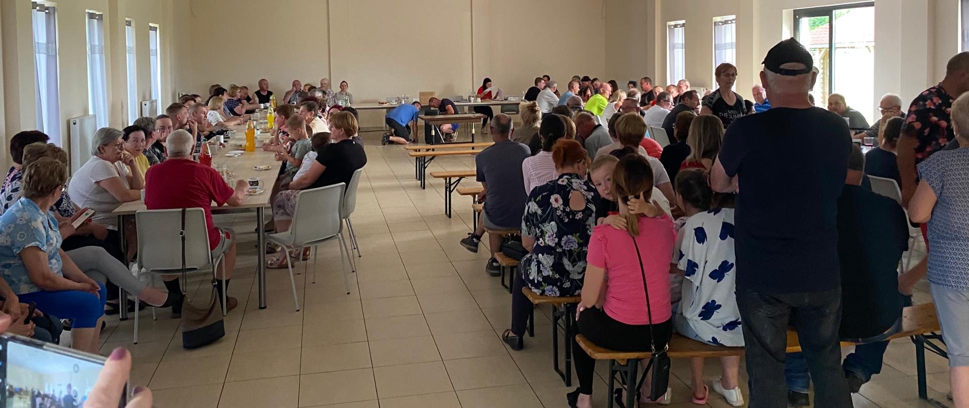 sala pełna siedzących na krzesłach i stojących ludzi