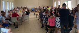 sala pełna siedzących na krzesłach i stojących ludzi