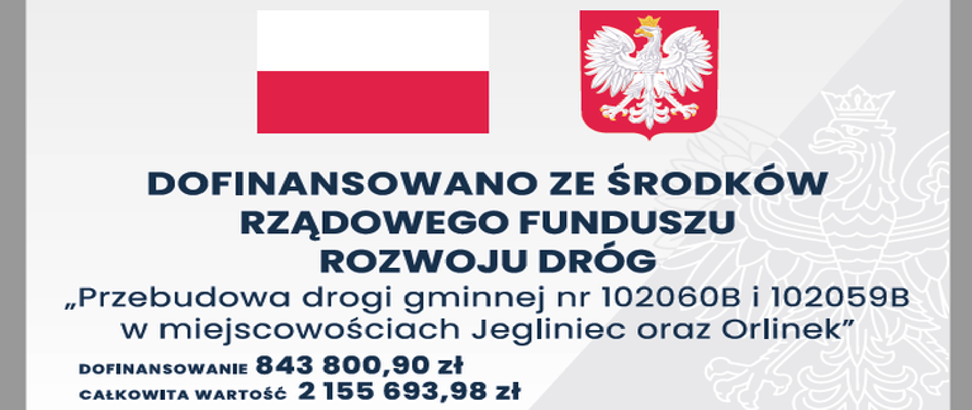 Tablica w kolorze biało-szarym, znak wodny orła, na górze po lewej stronie flaga Polski, po prawej godło, niżej napis "Dofinansowano ze środków Rządowego Rozwoju Dróg", poniżej napis: „Przebudowa drogi gminnej nr 102060B i 102059B w miejscowościach Jegliniec oraz Orlinek”