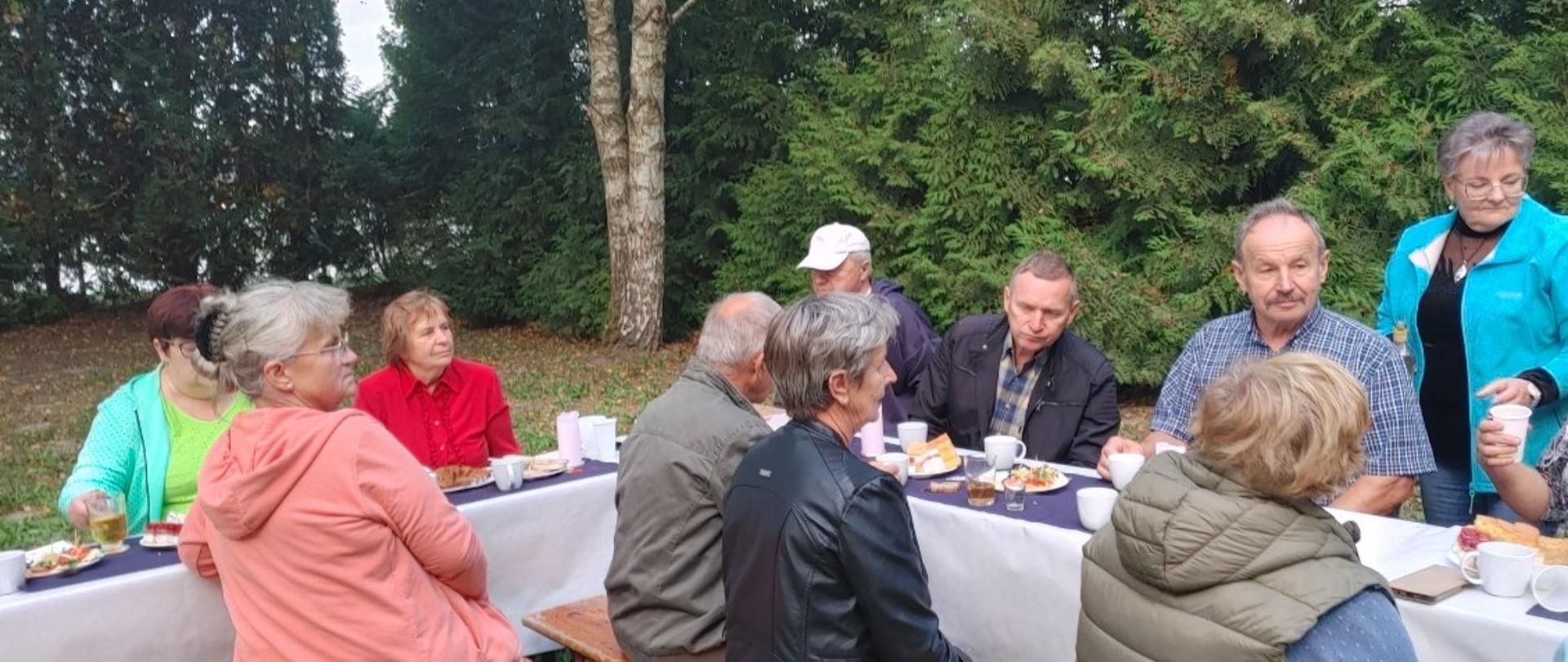 kobiety i mężczyźni siedzą przy wspólnym stole zastawionym różnymi smakołykami 