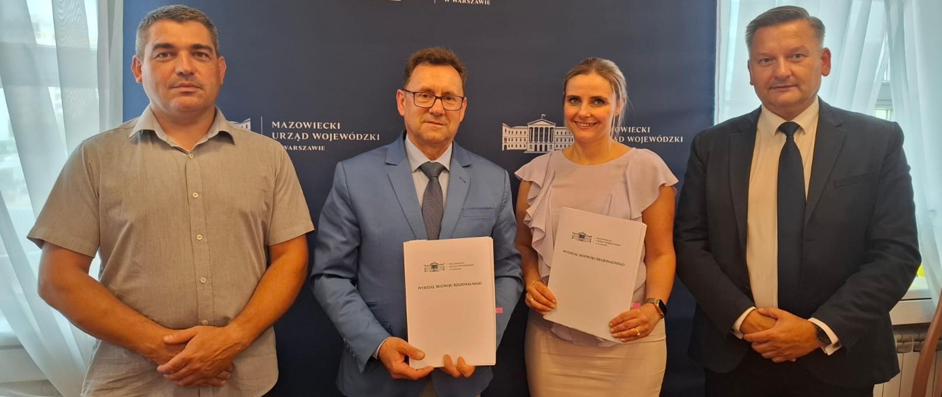 Na zdjęciu na tle ścianki osoby uczestniczące w uroczystości zgodnie z treścią artykułu. Starosta i przedstawiciel Wojewody Mazowieckiego trzymają w rękach podpisane egzemplarze umów.