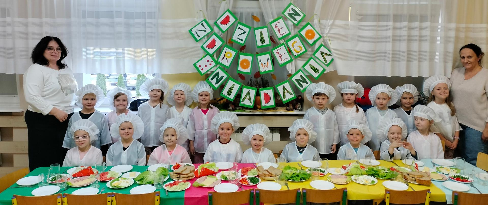 2 dorosłych im grupa dzieci w kucharskich ubraniach