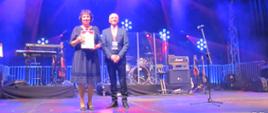 Na fotografii na tle oświetlonej sceny starosta Elżbieta Sadowska trzymająca w rękach otrzymany przez Powiat Sokołowski Dyplom za miejsce zajęte w rankingu Wspólnoty wraz z przedstawicielem organizatorów Gali.