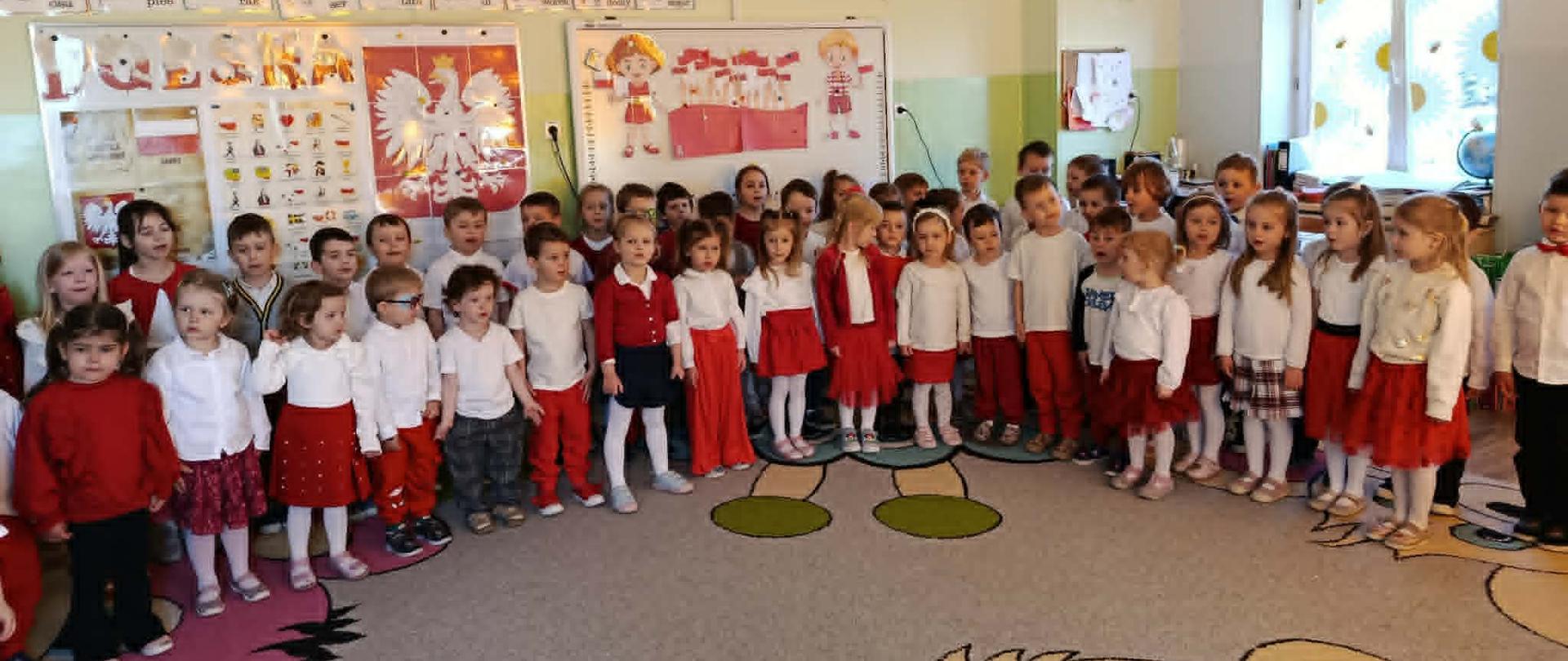 Grupa dzieci w odświętnych strojach śpiewa hymn