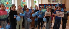 Uczniowie stoją w grupie, trzymają w rękach niebieskie balony, jeden z uczniów trzyma plakat z napisem "2 kwietnia Niebieskie Igrzyska"