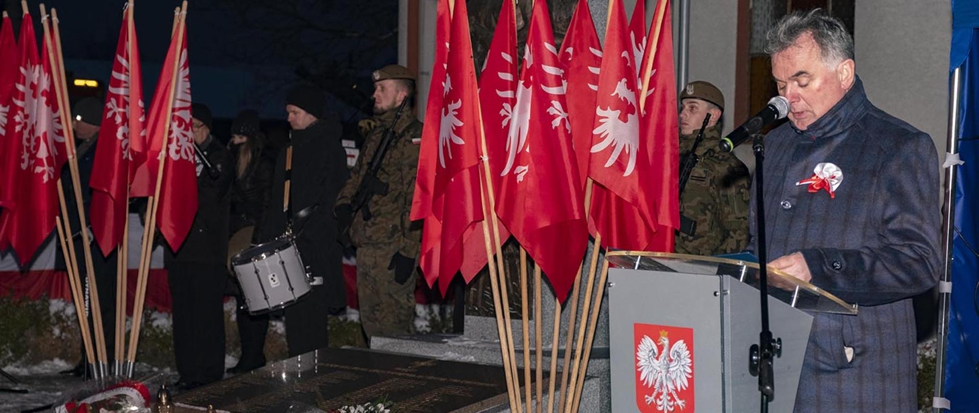burmistrz Miasta i Gminy Margonin przemawiający z mównicy, w tle flagi Powstania Wielkopolskiego, za nimi postacie w mundurach