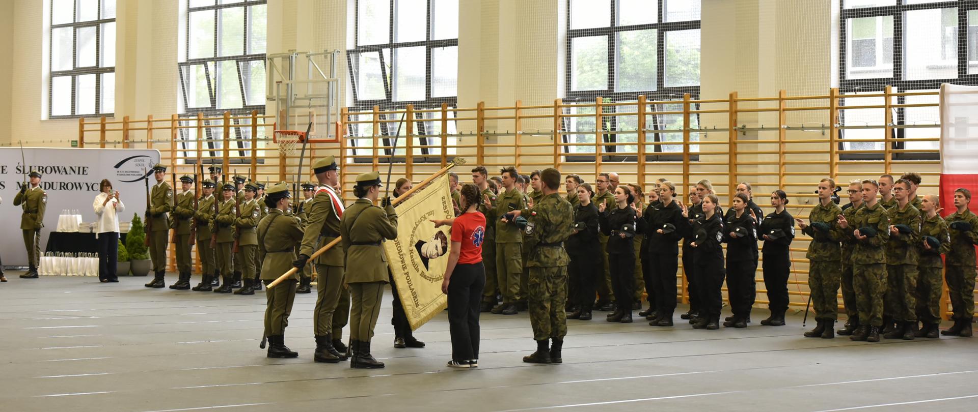 Na środku hali sportowej Uczniowie ślubują na sztandar w obecności oddziałów klas mundurowych.