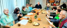 Uczestnicy spotkania siedzą przy stole, wspólnie kolędują