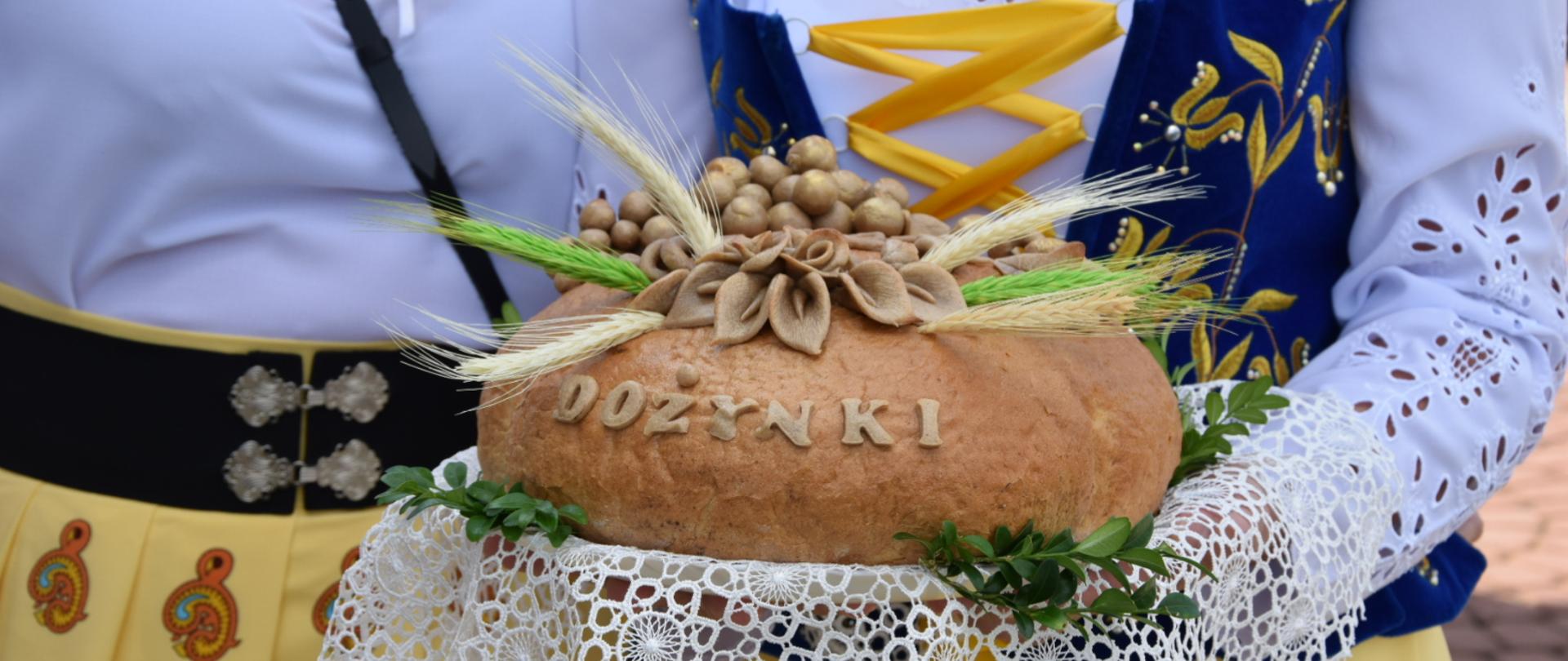 Bochen chleba z napisem dożynki trzymany przez parę góralską