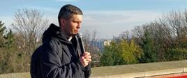 Ksiądz Maciej, organizator wycieczki modli się do mikrofonu, za nim mury klasztoru na jasnej Górze