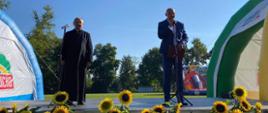 scena, na dole słoneczniki, po bokach namioty promocyjne gminy Wicko, przemawia Wójt Gminy Wicko wraz z księdzem Parafii Charbrowo