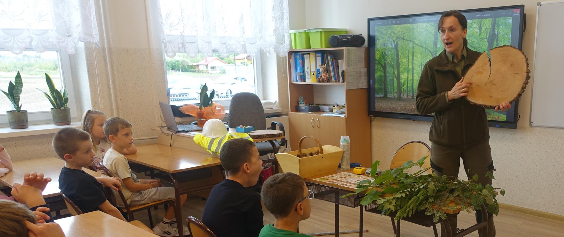 Uczniowie klas młodszych w sali lekcyjnej słuchają prelekcji Pani leśnik