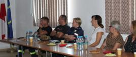 Uczestnicy konferencji siedzą przy biurku, przy monitorze zdalnym