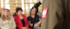 Przemawia przedstawiciel Wojskowego Centrum Rekrutacji w Bielsku Podlaskim - zdjęcie wykonane z perspektywy fragmentu wojskowego munduru z godłem Polski