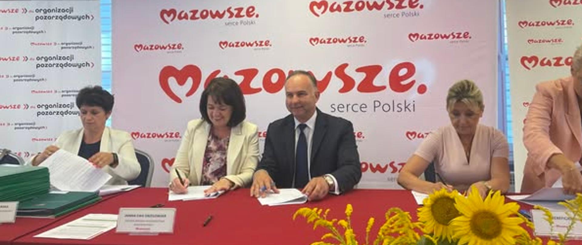 pięć osób siedzi za stołem nakrytym czerwonym suknem w trakcie podpisywania umów