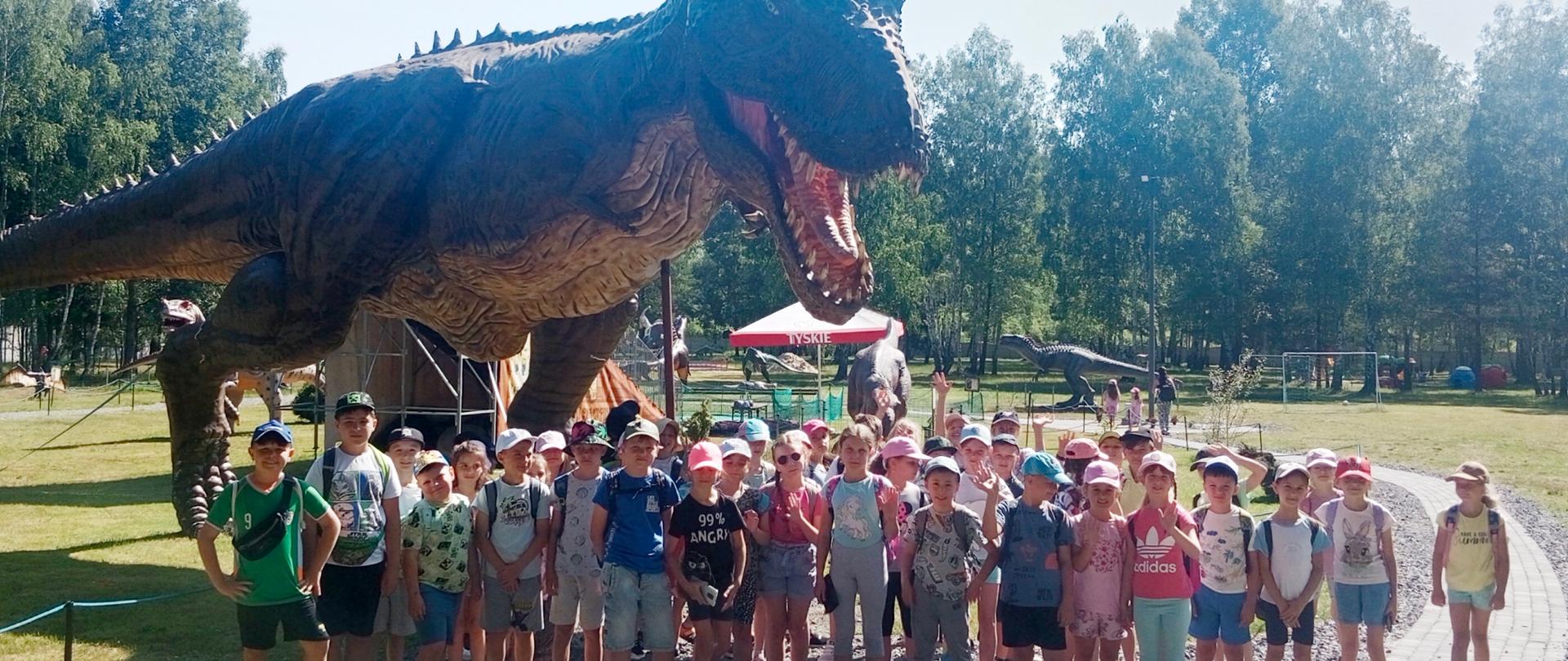 Uczniowie klas I A, I B i II A na tle dinozaura.